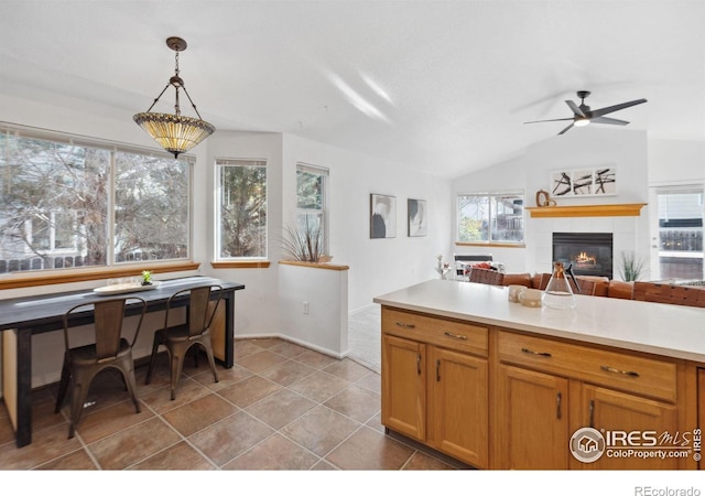 kitchen featuring pendant lighting, a fireplace, light countertops, a ceiling fan, and vaulted ceiling