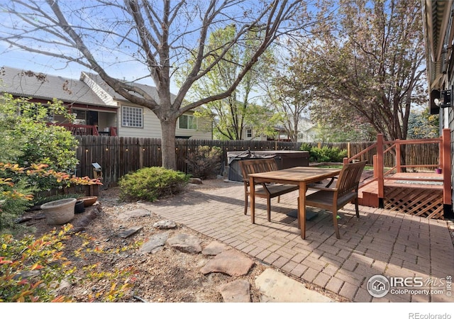 view of patio with a hot tub, a wooden deck, a fenced backyard, and outdoor dining space
