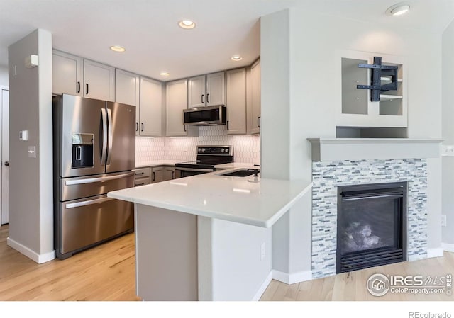 kitchen featuring gray cabinetry, light wood-style floors, appliances with stainless steel finishes, and a peninsula