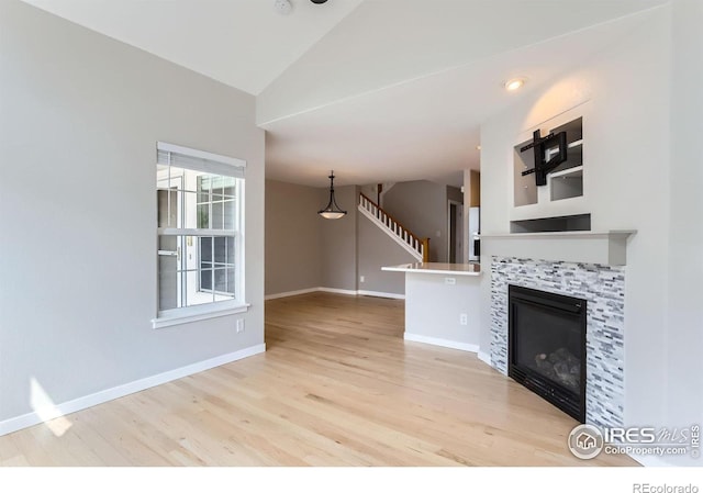 unfurnished living room featuring vaulted ceiling, wood finished floors, a tile fireplace, baseboards, and stairs