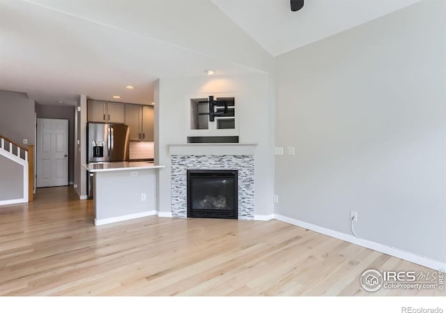 unfurnished living room featuring a fireplace, light wood-style flooring, baseboards, vaulted ceiling, and stairway