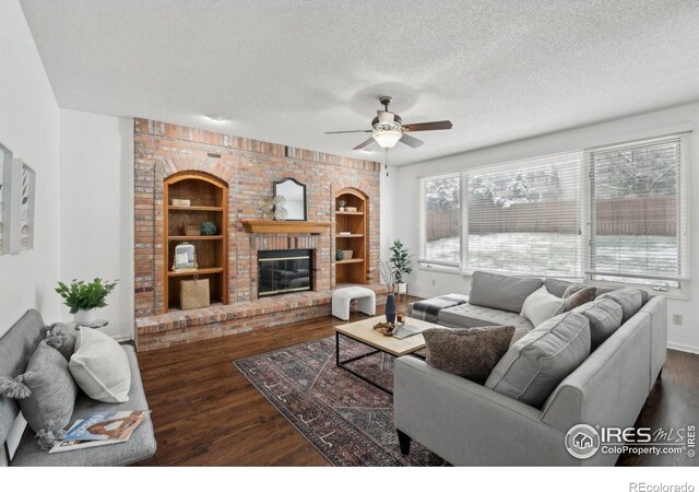 living room with ceiling fan, a brick fireplace, a textured ceiling, built in features, and wood finished floors