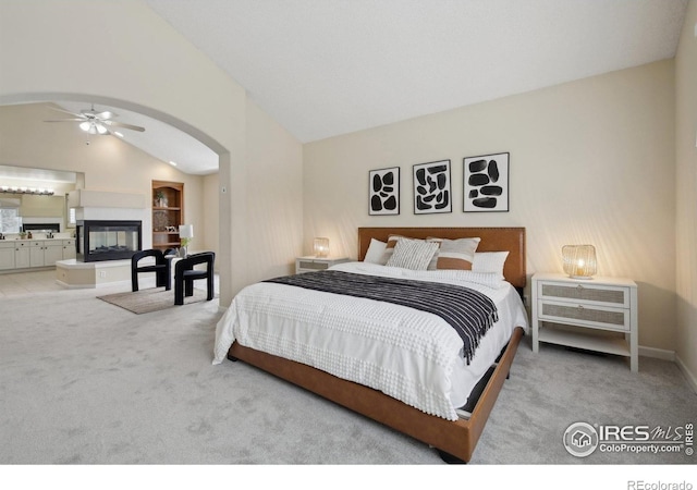 carpeted bedroom featuring arched walkways, a multi sided fireplace, ensuite bath, and high vaulted ceiling