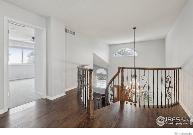 stairs featuring baseboards, visible vents, wood finished floors, and ceiling fan with notable chandelier