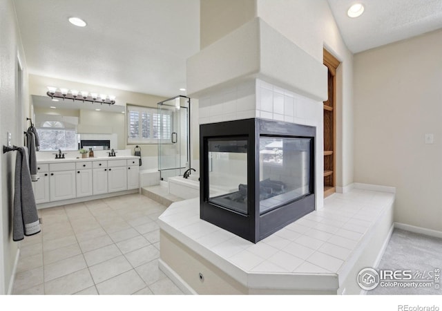 bathroom with double vanity, tile patterned flooring, a fireplace, a stall shower, and a sink