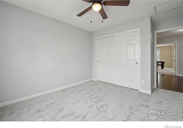 unfurnished bedroom featuring a ceiling fan, attic access, carpet floors, baseboards, and a closet