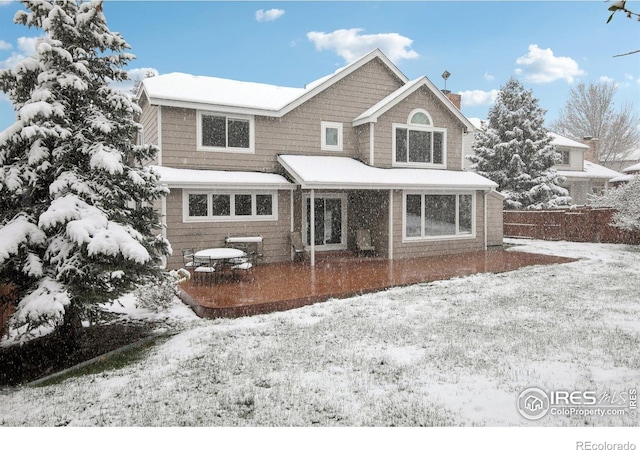 snow covered back of property featuring fence, a chimney, and a patio area