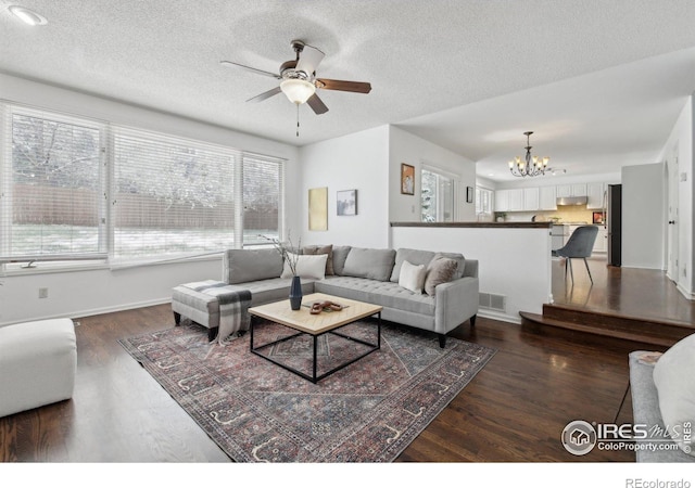living room with dark wood-style flooring, a textured ceiling, visible vents, and ceiling fan with notable chandelier