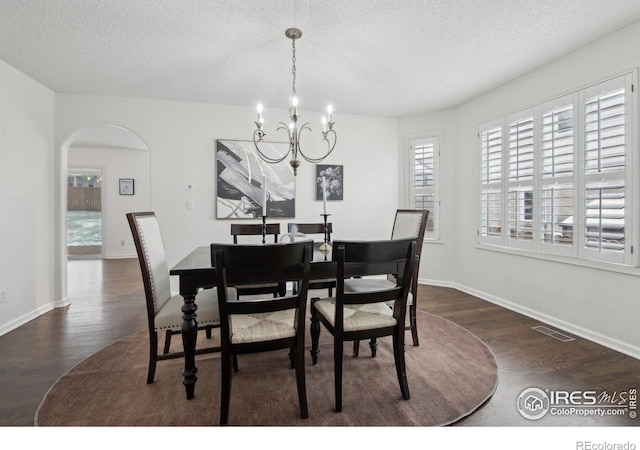 dining area featuring a textured ceiling, dark wood-style flooring, a chandelier, and a wealth of natural light