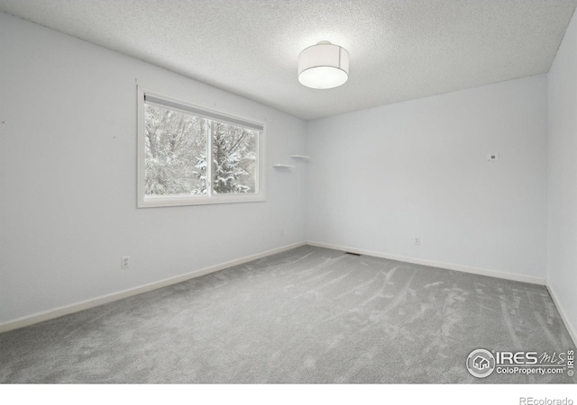 carpeted empty room featuring a textured ceiling and baseboards