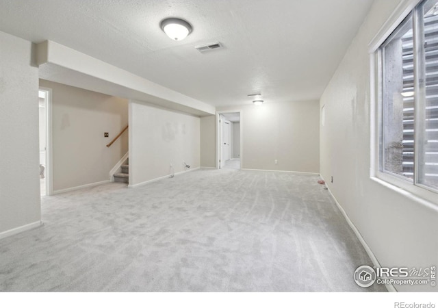 below grade area featuring a textured ceiling, visible vents, stairway, carpet floors, and baseboards