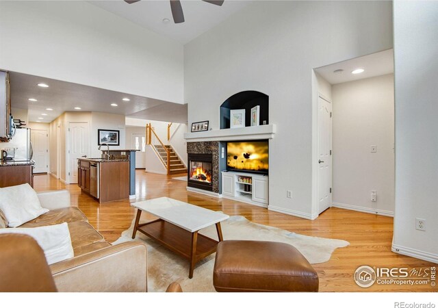 living room with a towering ceiling, baseboards, recessed lighting, a ceiling fan, and light wood-style flooring