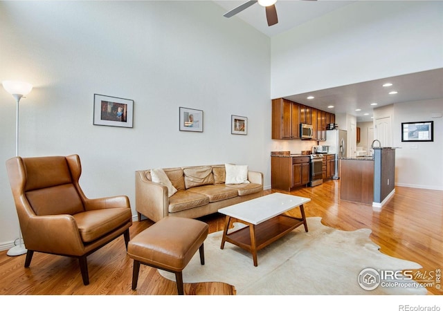 living room with baseboards, a high ceiling, a ceiling fan, and light wood-type flooring