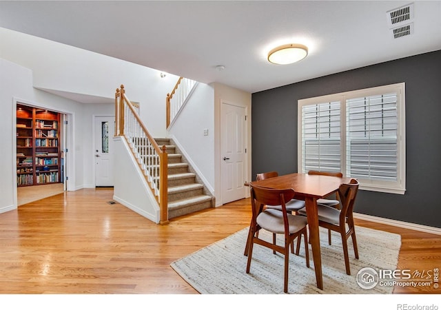 dining room with baseboards, light wood finished floors, visible vents, and stairway