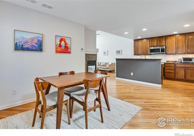 dining space featuring visible vents, a toaster, light wood finished floors, a glass covered fireplace, and recessed lighting