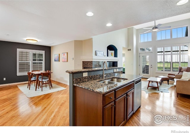 kitchen featuring stainless steel dishwasher, a sink, light wood finished floors, and open floor plan