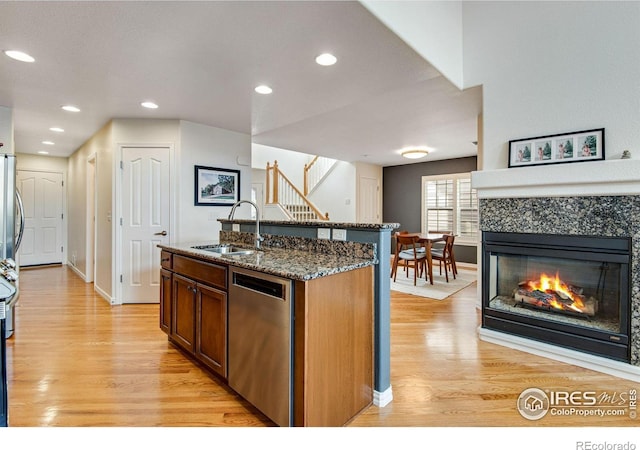 kitchen featuring baseboards, light wood-type flooring, a sink, dark stone countertops, and dishwasher