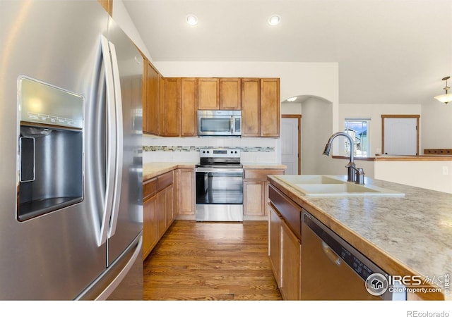 7056 Langland St, Wellington, CO 80549 - kitchen with appliances with stainless steel finishes, a sink, arched walkways, brown cabinetry, and dark wood-style flooring