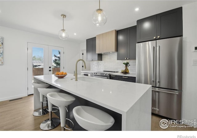 kitchen featuring a sink, stainless steel appliances, wood finished floors, tasteful backsplash, and a center island with sink