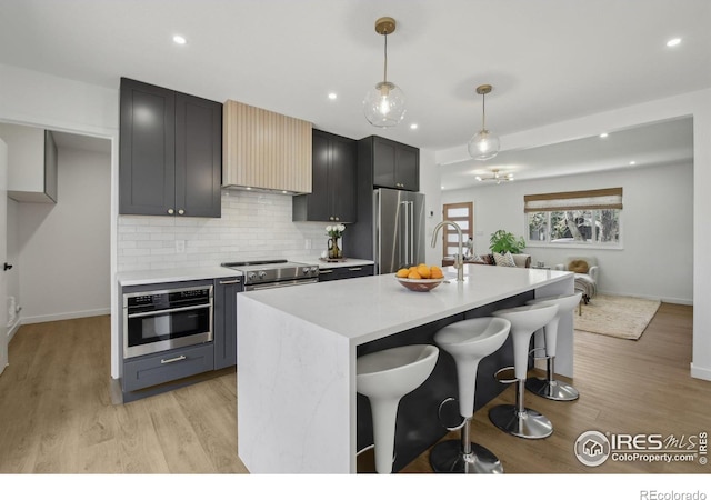 kitchen featuring a kitchen bar, light countertops, light wood-style flooring, appliances with stainless steel finishes, and backsplash