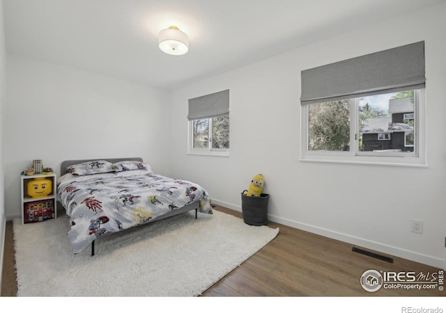 bedroom with baseboards, visible vents, multiple windows, and wood finished floors