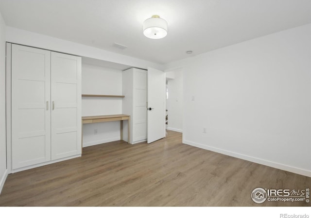 unfurnished bedroom with built in study area, baseboards, light wood-type flooring, visible vents, and a closet