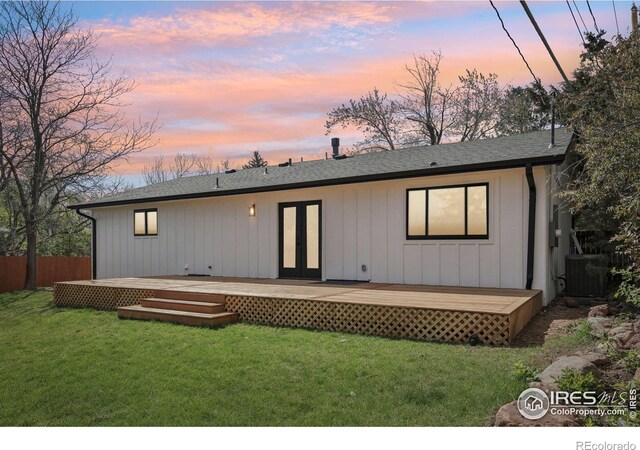 back of property featuring french doors, a lawn, a wooden deck, fence, and a shingled roof