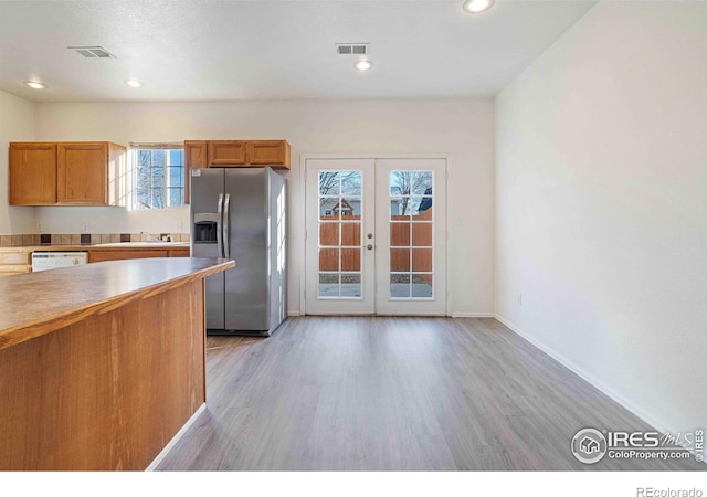 kitchen with visible vents, light wood-style floors, baseboards, stainless steel fridge with ice dispenser, and french doors