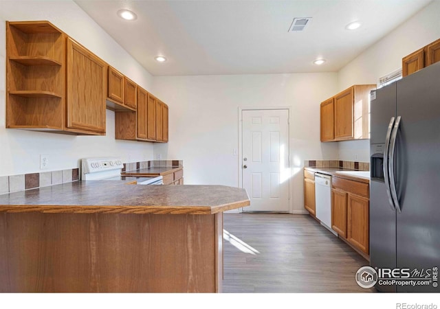 kitchen with brown cabinetry, a peninsula, wood finished floors, white appliances, and recessed lighting