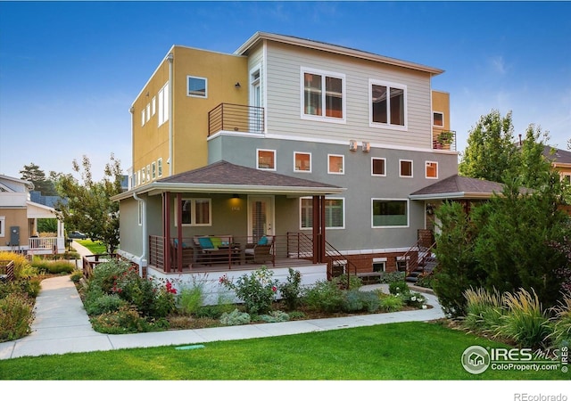 view of front of property featuring covered porch, stucco siding, a front lawn, and a balcony