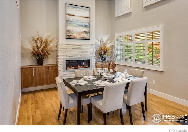 dining room with baseboards, a stone fireplace, and wood finished floors