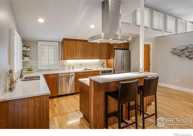 kitchen with island range hood, brown cabinets, a sink, light wood finished floors, and stainless steel appliances