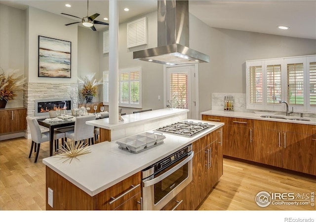 kitchen with island exhaust hood, appliances with stainless steel finishes, a center island, brown cabinets, and a sink