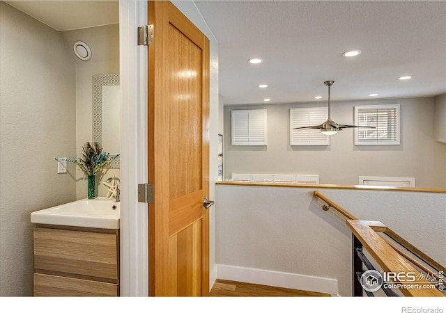 interior space featuring wood finished floors, baseboards, recessed lighting, a sink, and an upstairs landing