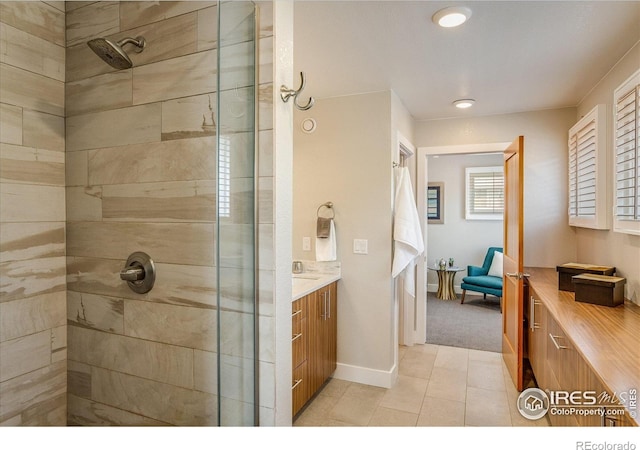 full bath with vanity, tile patterned flooring, baseboards, and a tile shower