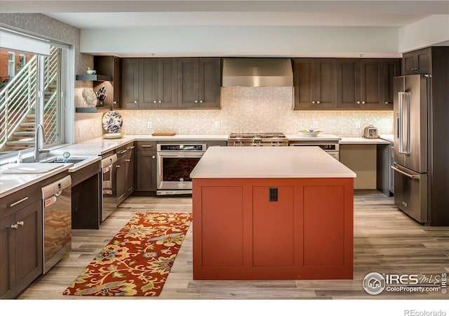 kitchen featuring wall chimney range hood, a center island, light wood-style floors, and stainless steel appliances