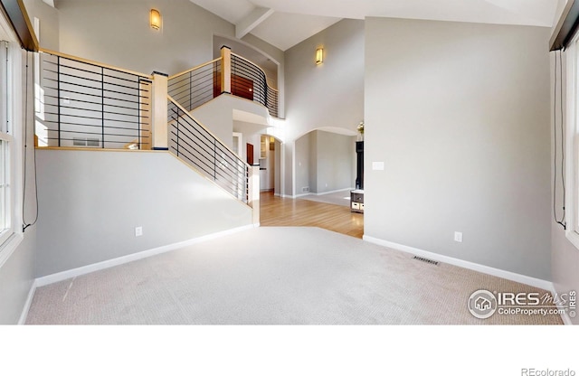 interior space with carpet floors, arched walkways, high vaulted ceiling, and baseboards