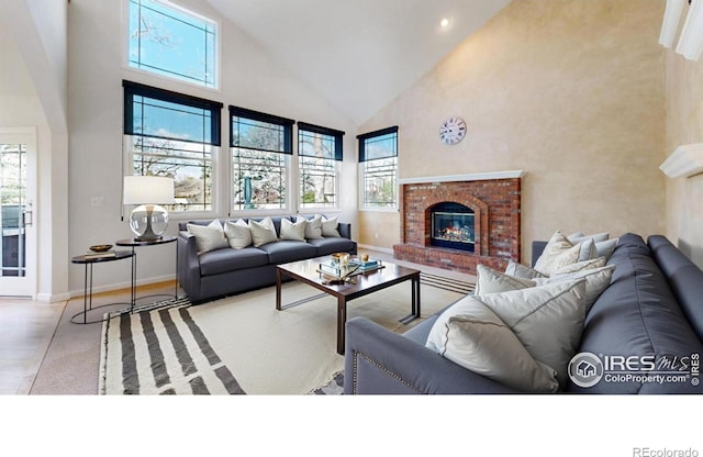 living area featuring a healthy amount of sunlight, high vaulted ceiling, baseboards, and a brick fireplace