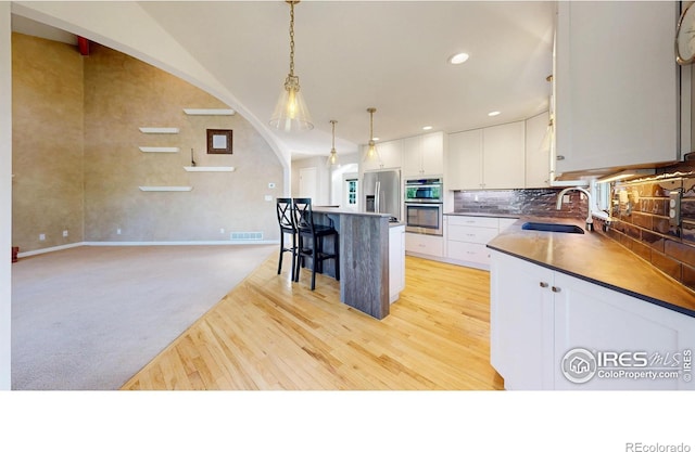 kitchen featuring visible vents, a kitchen bar, a sink, light wood finished floors, and appliances with stainless steel finishes