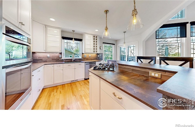 kitchen with dark countertops, appliances with stainless steel finishes, a sink, light wood-type flooring, and tasteful backsplash