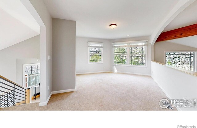 unfurnished room with baseboards, carpet flooring, arched walkways, and a wealth of natural light