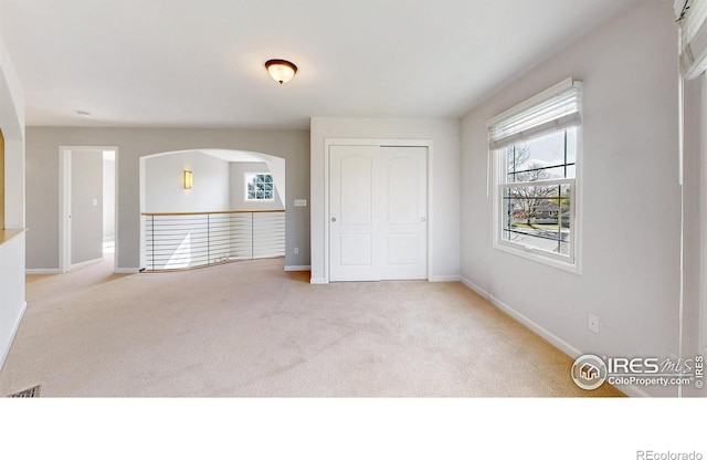 unfurnished bedroom with baseboards, carpet, and arched walkways