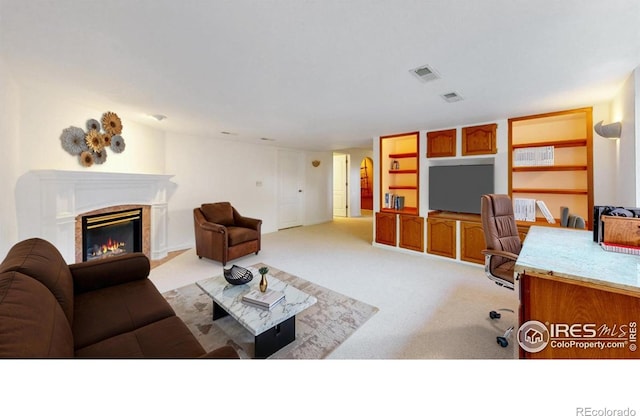 living room featuring a glass covered fireplace, built in features, light carpet, and visible vents