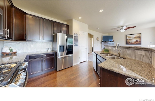 kitchen with appliances with stainless steel finishes, a sink, arched walkways, decorative backsplash, and wood finished floors