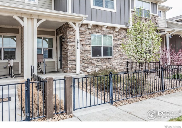 doorway to property with covered porch, board and batten siding, a gate, and stone siding
