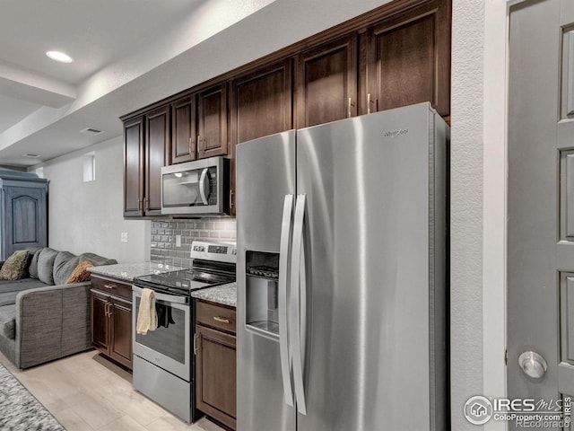 kitchen featuring decorative backsplash, dark brown cabinets, light stone countertops, open floor plan, and appliances with stainless steel finishes