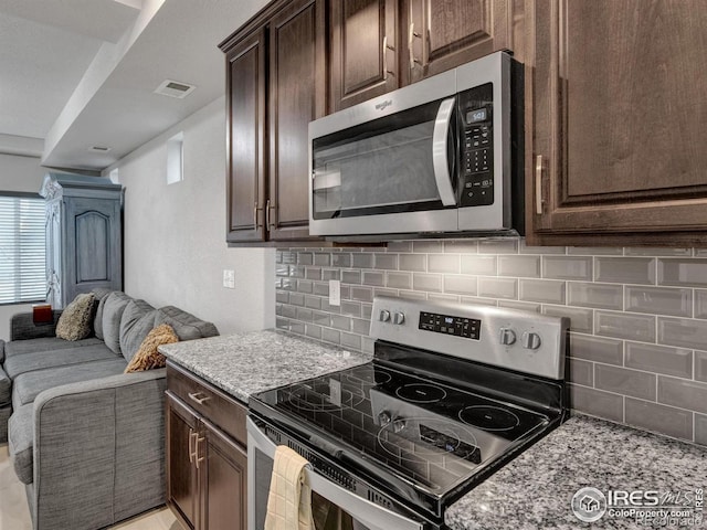 kitchen with dark brown cabinetry, stainless steel appliances, open floor plan, tasteful backsplash, and visible vents