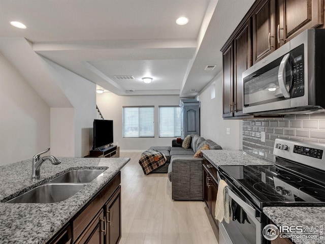 kitchen featuring a sink, appliances with stainless steel finishes, light stone counters, and a raised ceiling