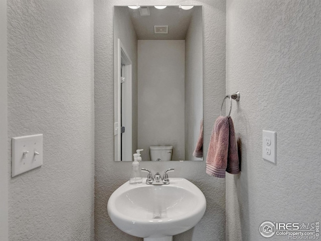 bathroom with a sink, a textured wall, and toilet