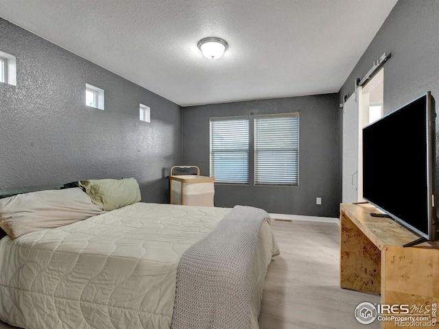 bedroom featuring a textured ceiling, light wood-type flooring, a barn door, baseboards, and a textured wall